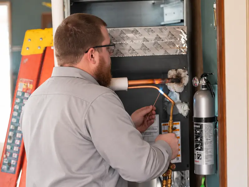 Little Dillo technician brazing copper refrigerant lines on an indoor HVAC coil during an installation