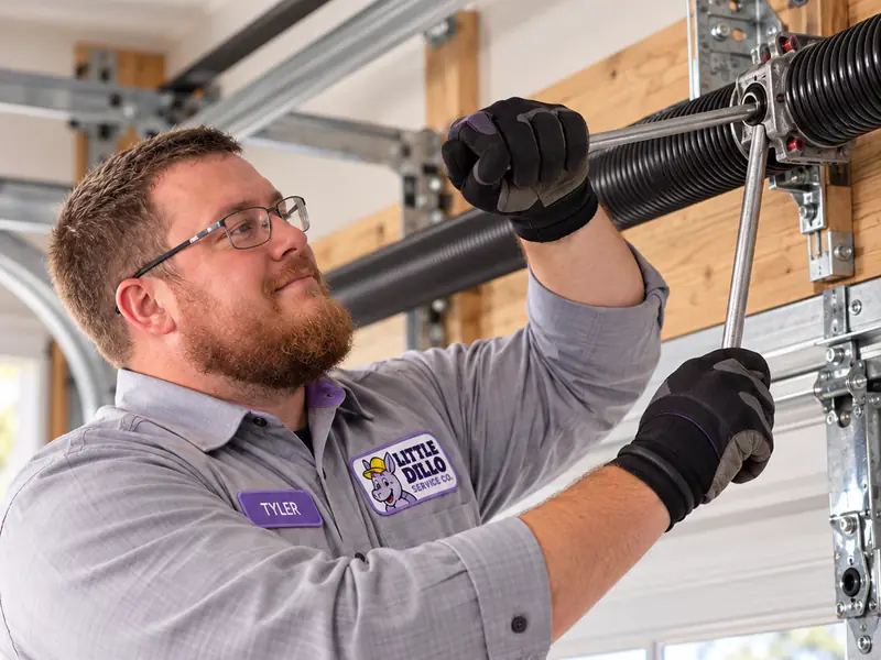 Little Dillo technician adjusting a garage door torsion spring with winding bars